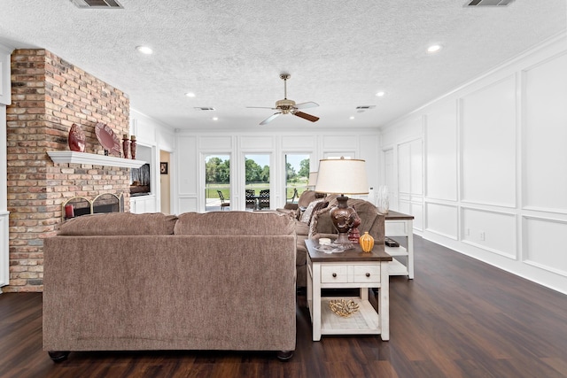 living room with a textured ceiling, ceiling fan, crown molding, a fireplace, and dark hardwood / wood-style floors