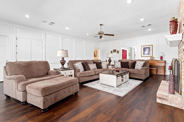 living room featuring dark wood-type flooring, crown molding, a brick fireplace, ceiling fan, and a textured ceiling