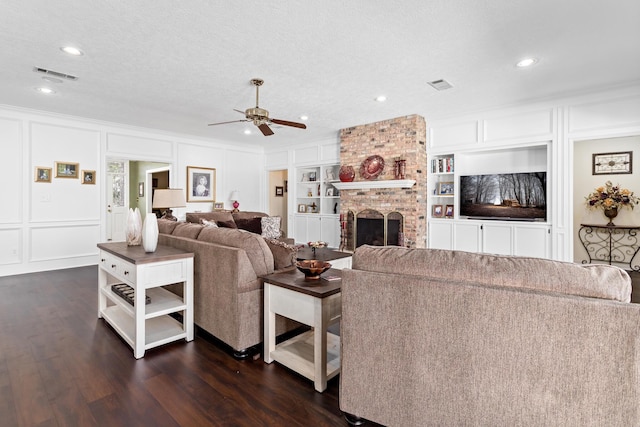 living room featuring dark hardwood / wood-style flooring, a brick fireplace, built in shelves, a textured ceiling, and ceiling fan