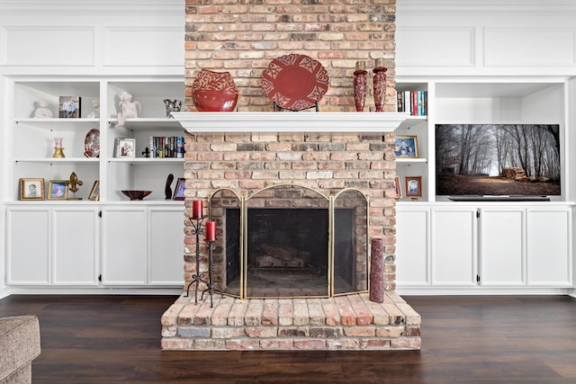 living room featuring built in shelves, dark hardwood / wood-style floors, and a brick fireplace