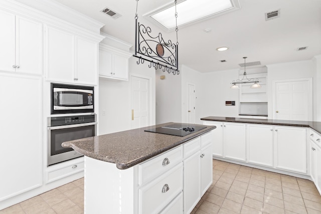 kitchen with appliances with stainless steel finishes, dark stone counters, light tile patterned floors, white cabinets, and a center island