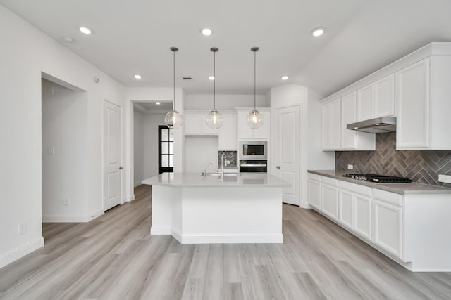 kitchen with white cabinetry, built in microwave, oven, decorative light fixtures, and a kitchen island with sink