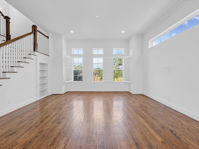 unfurnished living room with plenty of natural light, ornamental molding, dark hardwood / wood-style floors, and built in shelves