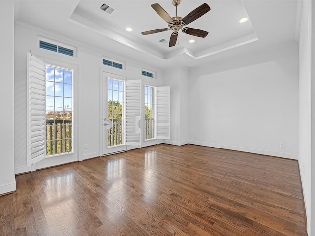 empty room with dark wood-type flooring, ceiling fan, ornamental molding, and a raised ceiling