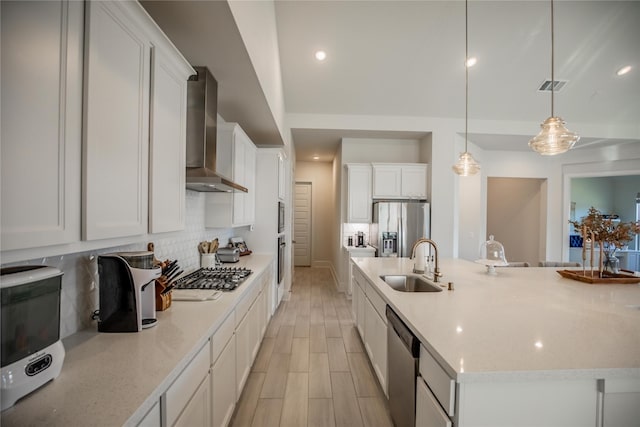 kitchen with wall chimney exhaust hood, stainless steel appliances, sink, pendant lighting, and a center island with sink