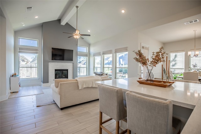 living room featuring beamed ceiling, a healthy amount of sunlight, and ceiling fan with notable chandelier