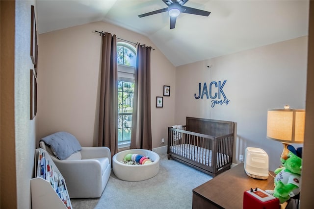 carpeted bedroom featuring a nursery area, lofted ceiling, and ceiling fan