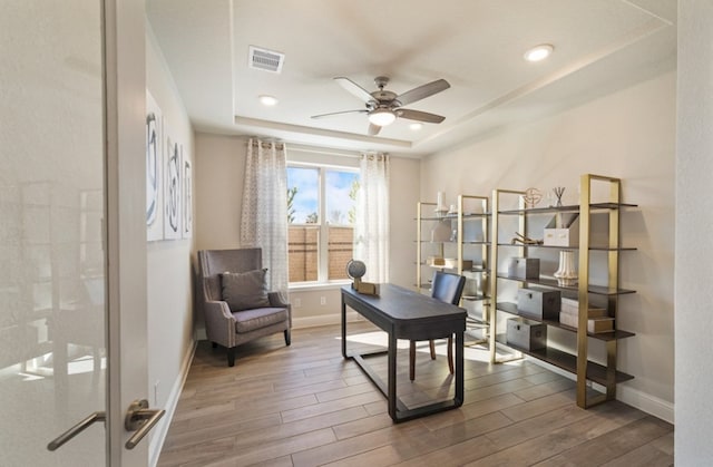 office space featuring a tray ceiling, visible vents, a ceiling fan, wood finished floors, and baseboards