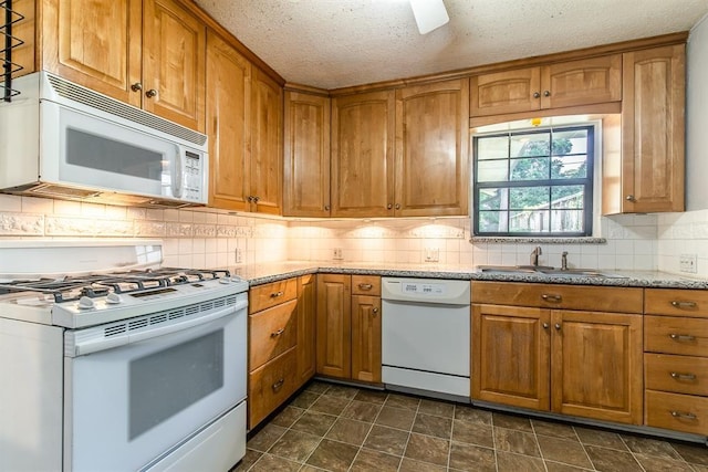 kitchen with a textured ceiling, light stone counters, sink, and white appliances