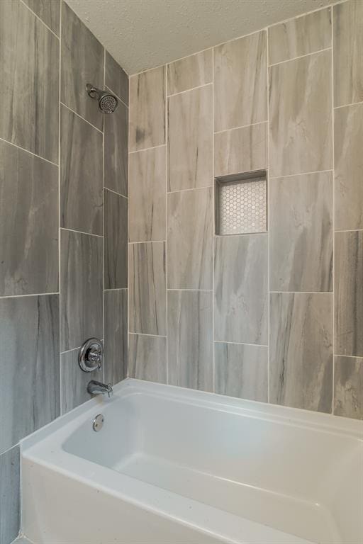 bathroom featuring a textured ceiling and tiled shower / bath