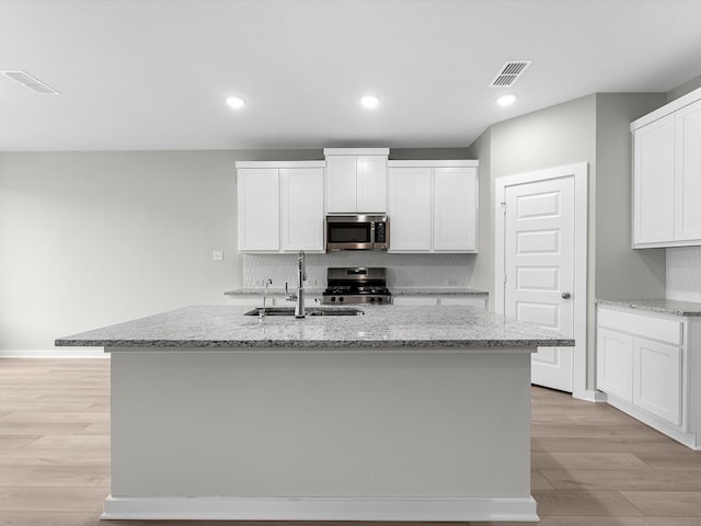 kitchen featuring stainless steel appliances, an island with sink, light stone counters, sink, and white cabinetry