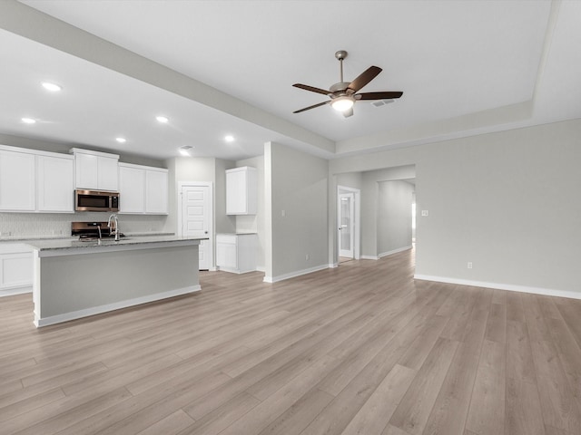 unfurnished living room with a tray ceiling, sink, ceiling fan, and light hardwood / wood-style flooring