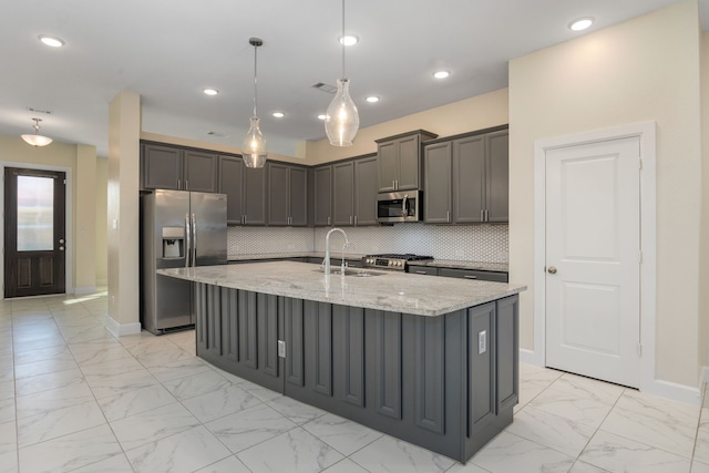 kitchen with light stone countertops, appliances with stainless steel finishes, a kitchen island with sink, and sink