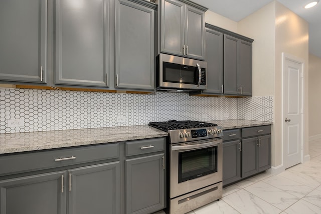 kitchen with decorative backsplash, gray cabinets, light stone countertops, and stainless steel appliances