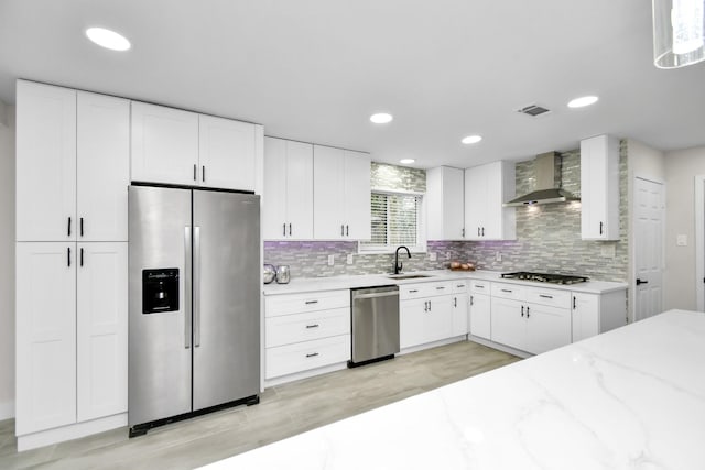 kitchen with light stone countertops, white cabinets, stainless steel appliances, and wall chimney range hood