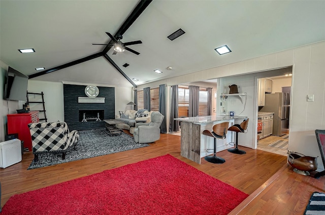 living room with ceiling fan, a fireplace, lofted ceiling with beams, and light hardwood / wood-style floors