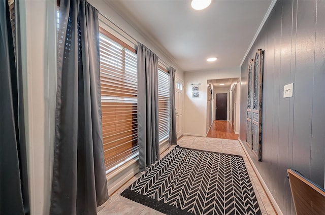 hallway featuring wooden walls, crown molding, and light tile patterned floors