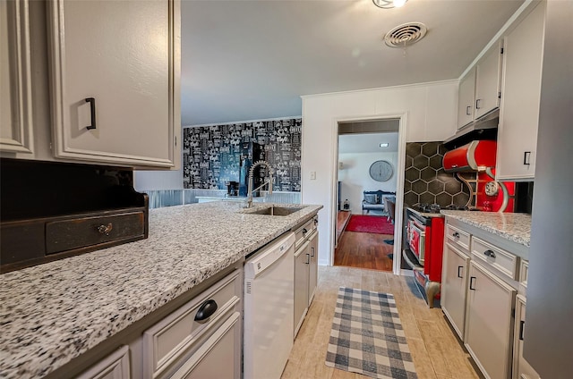 kitchen featuring white dishwasher, sink, light hardwood / wood-style floors, light stone counters, and range