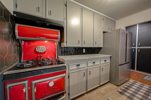 kitchen with stove, light wood-type flooring, backsplash, and stainless steel refrigerator