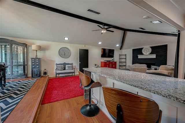 kitchen with light stone countertops, ceiling fan, a fireplace, vaulted ceiling with beams, and light hardwood / wood-style floors