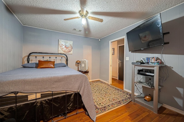 bedroom featuring ceiling fan, wood walls, wood-type flooring, and a textured ceiling