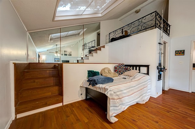 bedroom featuring hardwood / wood-style floors, a skylight, and high vaulted ceiling