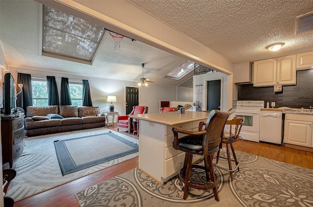 kitchen with a breakfast bar, white cabinetry, white appliances, and ceiling fan