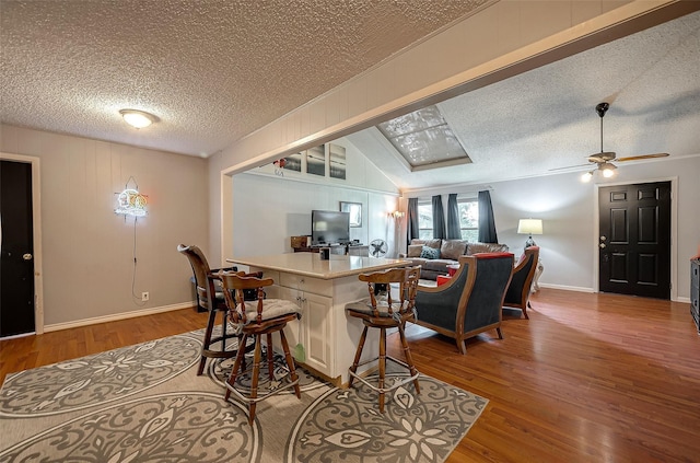 kitchen featuring ceiling fan, light hardwood / wood-style floors, a kitchen bar, and vaulted ceiling