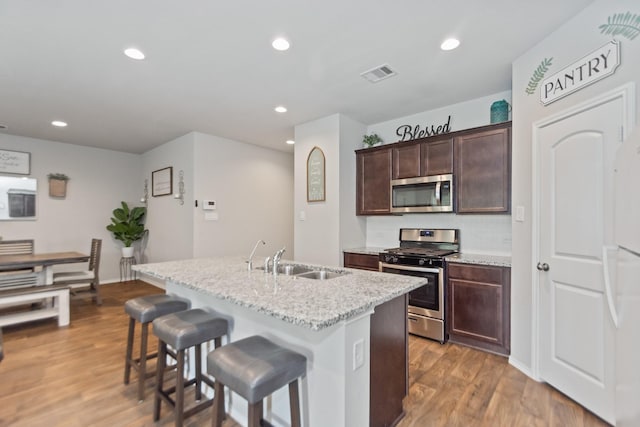 kitchen featuring wood finished floors, visible vents, a sink, appliances with stainless steel finishes, and a kitchen bar