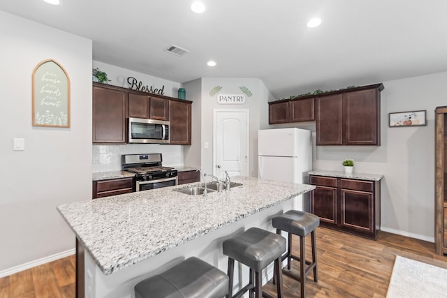 kitchen with dark brown cabinets, a breakfast bar, wood finished floors, stainless steel appliances, and a sink