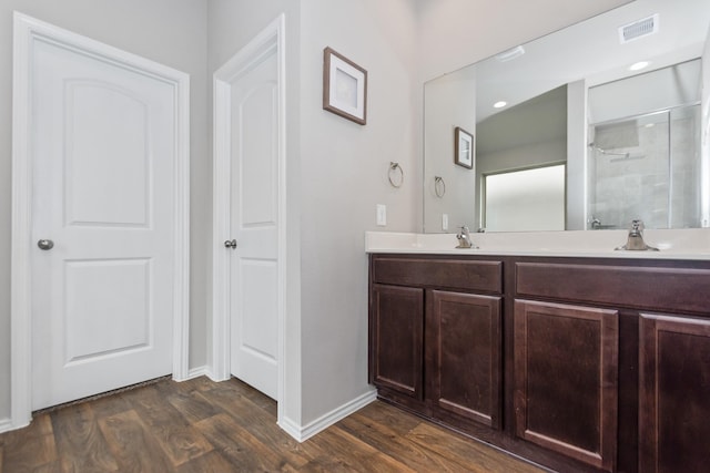 full bathroom featuring visible vents, a shower with door, a sink, wood finished floors, and double vanity