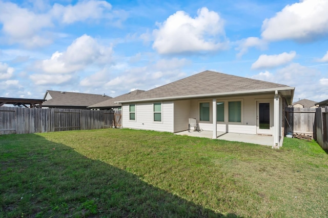 rear view of house with a shingled roof, a lawn, a fenced backyard, and a patio area