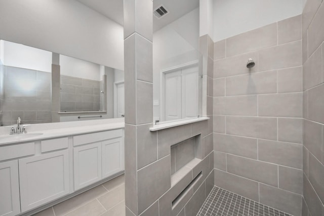 bathroom featuring visible vents, a tile shower, and vanity