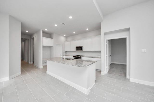 kitchen featuring light tile patterned floors, stainless steel appliances, a sink, white cabinetry, and a center island with sink