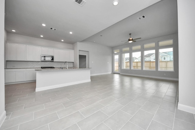 kitchen featuring stainless steel microwave, visible vents, backsplash, open floor plan, and white cabinetry