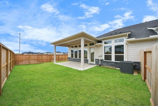 rear view of house with central AC unit, a fenced backyard, stone siding, a lawn, and a patio area