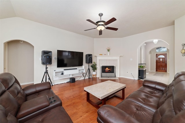 living room featuring hardwood / wood-style floors, ceiling fan, lofted ceiling, and a tile fireplace