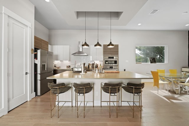 kitchen featuring a kitchen island with sink, stainless steel appliances, wall chimney exhaust hood, and white cabinets