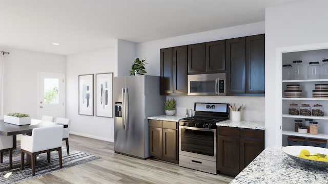 kitchen with dark brown cabinets, light stone countertops, appliances with stainless steel finishes, and light hardwood / wood-style flooring