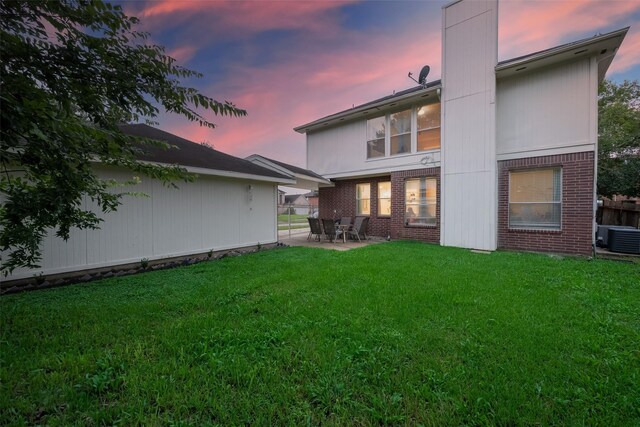 back house at dusk featuring a lawn, cooling unit, and a patio area