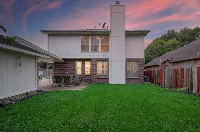 back house at dusk featuring a lawn and a patio area