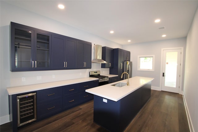 kitchen featuring a kitchen island with sink, wall chimney range hood, sink, appliances with stainless steel finishes, and beverage cooler