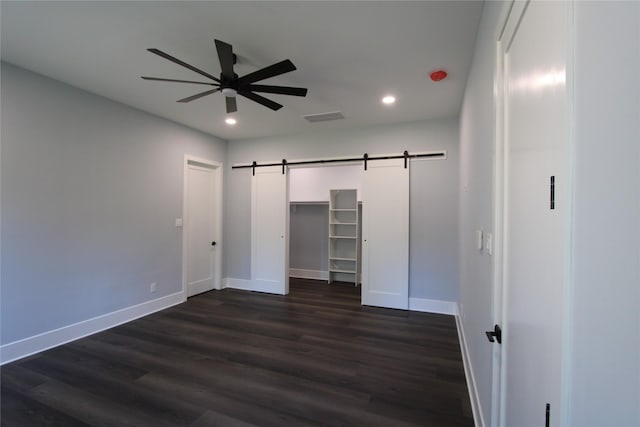 unfurnished bedroom with dark hardwood / wood-style flooring, ceiling fan, a barn door, a spacious closet, and a closet