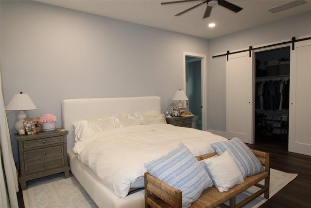 bedroom featuring a walk in closet, ceiling fan, a barn door, light wood-type flooring, and a closet