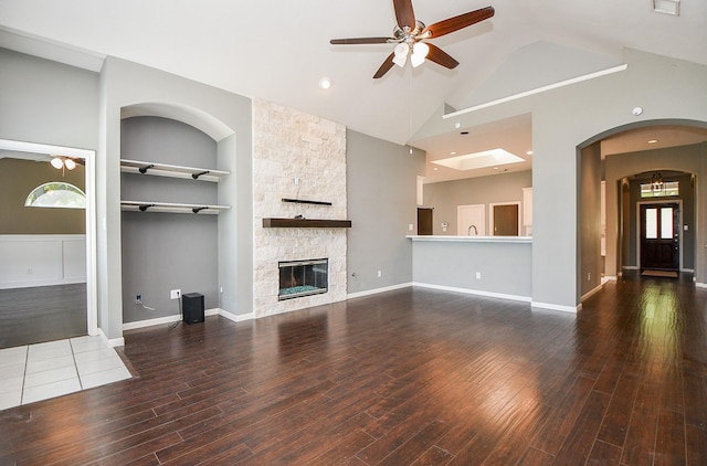 unfurnished living room featuring built in shelves, dark hardwood / wood-style flooring, a stone fireplace, and a healthy amount of sunlight