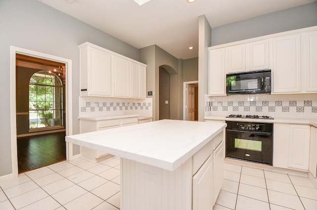 kitchen featuring tasteful backsplash, black appliances, light tile patterned floors, a center island, and white cabinetry