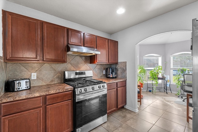 kitchen with decorative backsplash, stainless steel gas range oven, and light tile patterned flooring