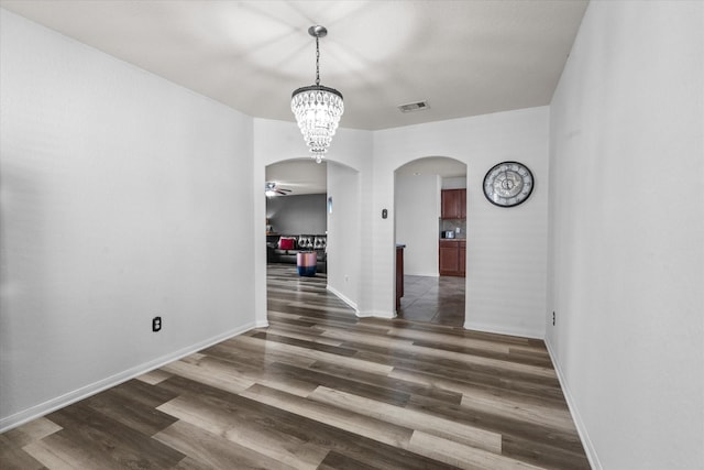 unfurnished dining area featuring ceiling fan with notable chandelier and dark wood-type flooring