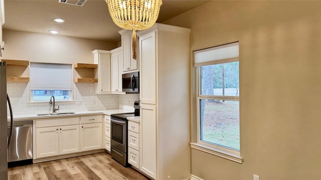 kitchen with decorative light fixtures, sink, white cabinetry, light wood-type flooring, and appliances with stainless steel finishes