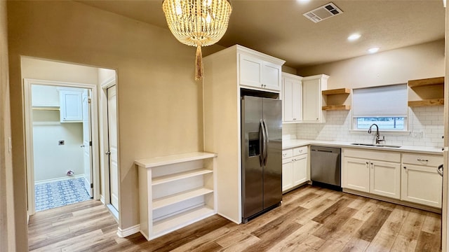 kitchen featuring appliances with stainless steel finishes, decorative light fixtures, white cabinetry, light hardwood / wood-style floors, and sink